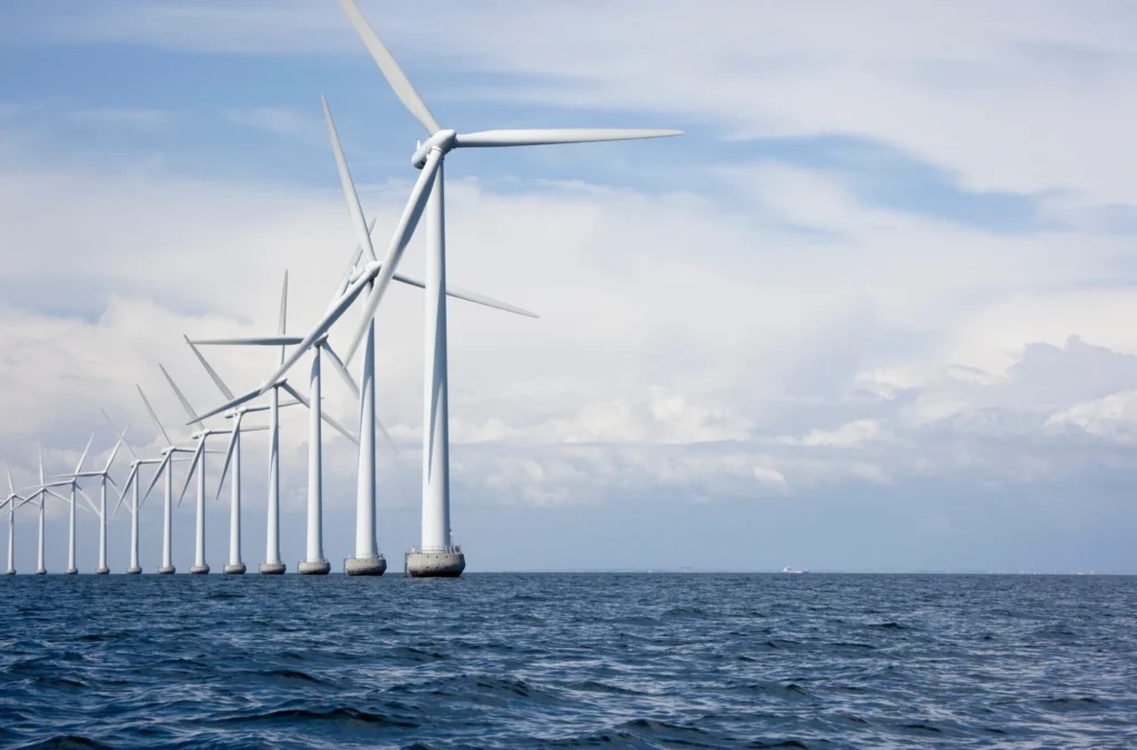 A row of offshore wind turbines stands in the sea beneath a partly cloudy sky, generating renewable energy.